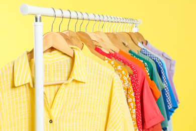 Bright clothes hanging on rack against yellow background, closeup. Rainbow colors