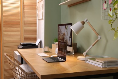 Photo of Stylish workplace with computer, laptop and lamp near olive wall at home