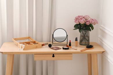 Photo of Mirror, cosmetic products, box of jewelry and vase with pink roses on wooden dressing table in makeup room