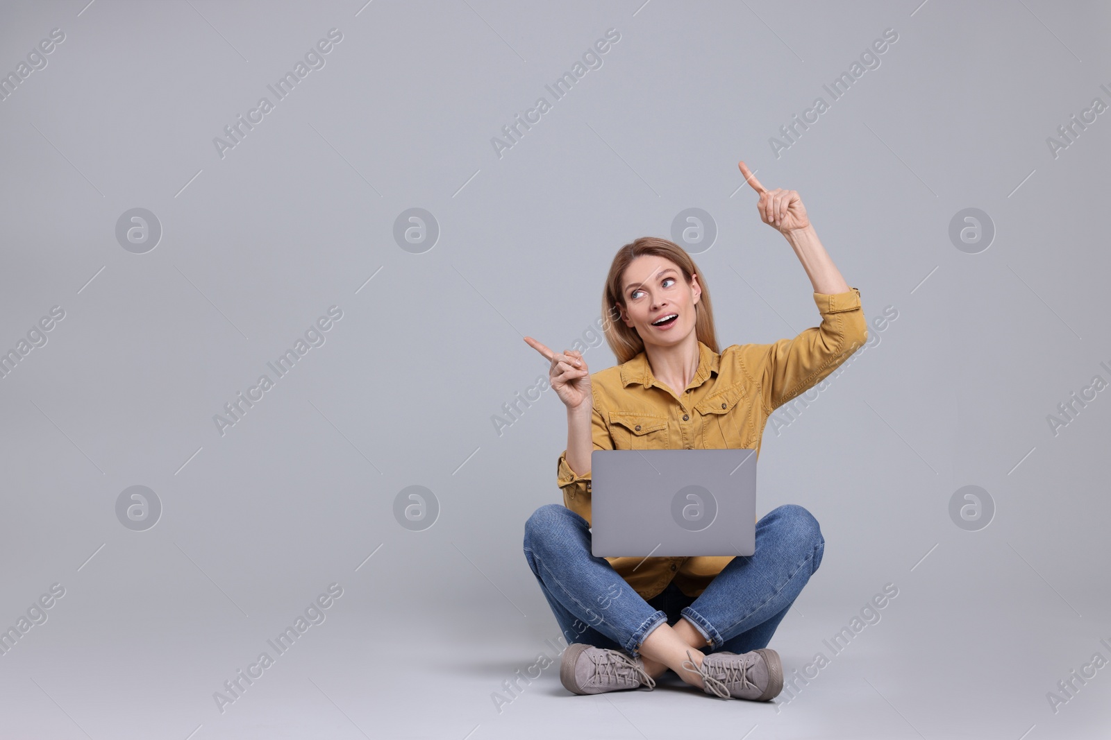 Photo of Happy woman with laptop pointing at something on light grey background. Space for text