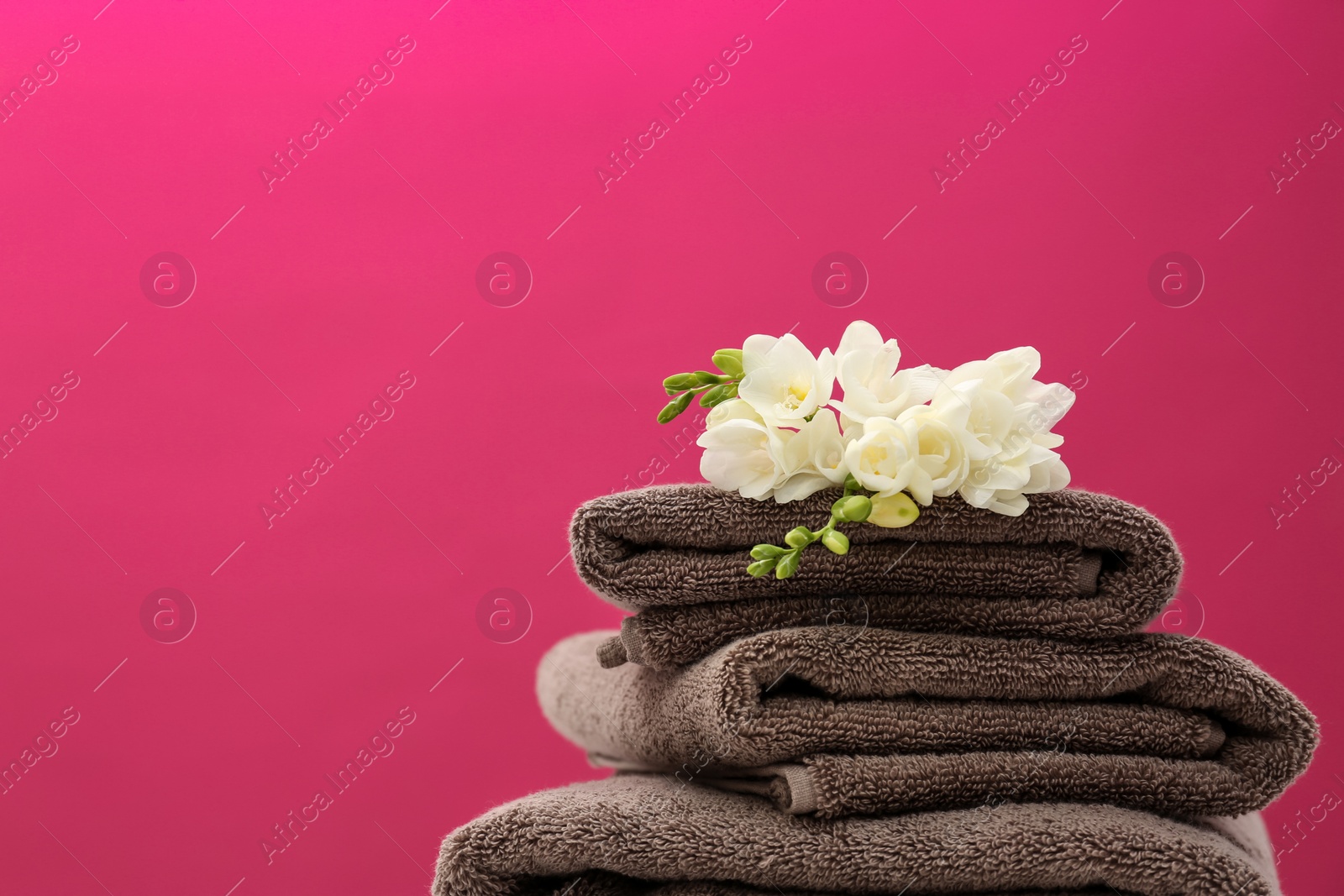 Photo of Stack of soft clean towels with beautiful flowers on color background. Space for text