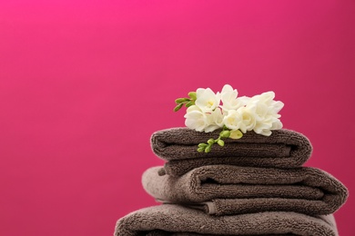 Photo of Stack of soft clean towels with beautiful flowers on color background. Space for text