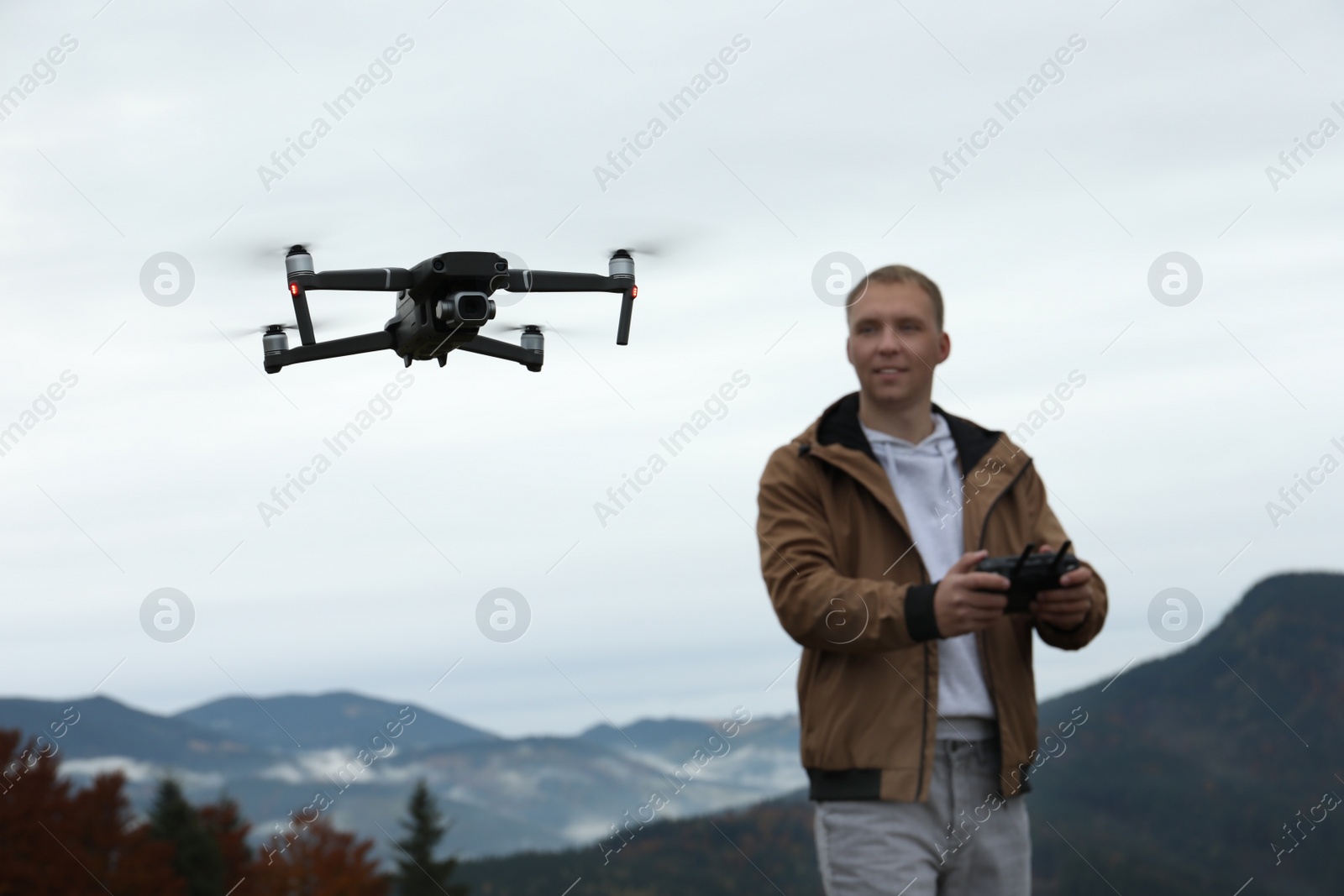 Photo of Young man operating modern drone with remote control in mountains