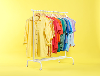 Photo of Bright clothes hanging on rack against yellow background. Rainbow colors