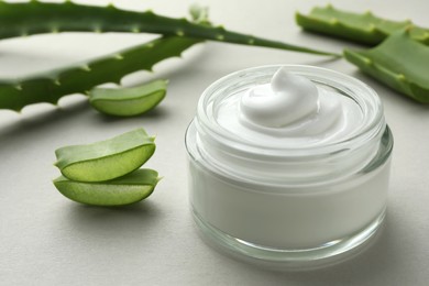 Photo of Jar with cream and cut aloe leaves on light grey background, closeup