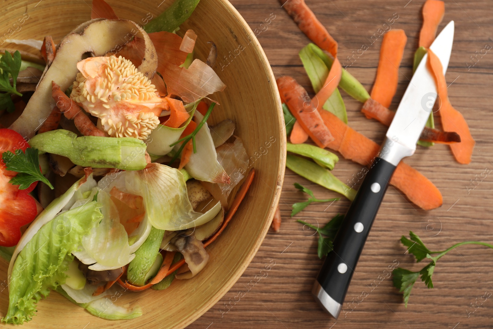 Photo of Peels of fresh vegetables and knife on wooden table, flat lay