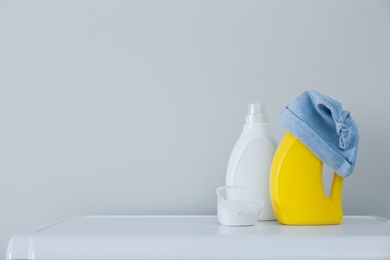 Photo of Detergents and children's hat on white table near wall. Space for text