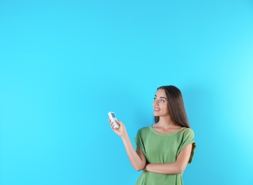 Young woman switching on air conditioner on color background