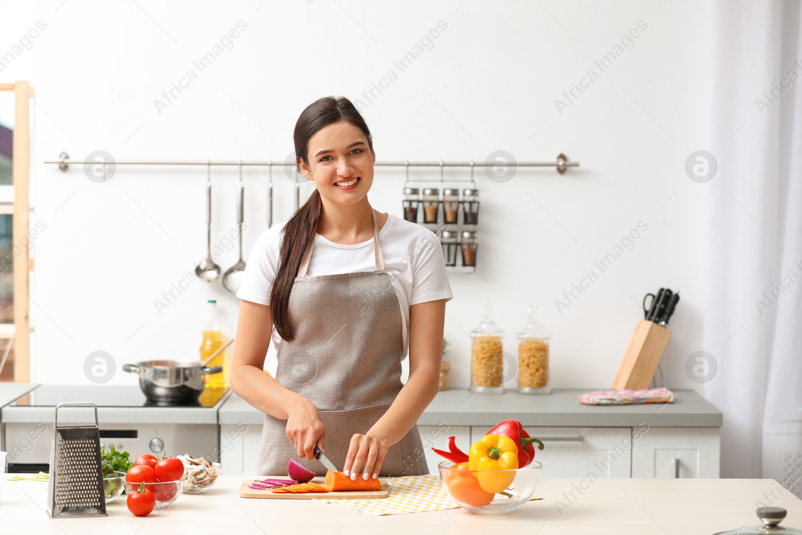 Photo of Young woman cutting vegetables for soup at table in kitchen