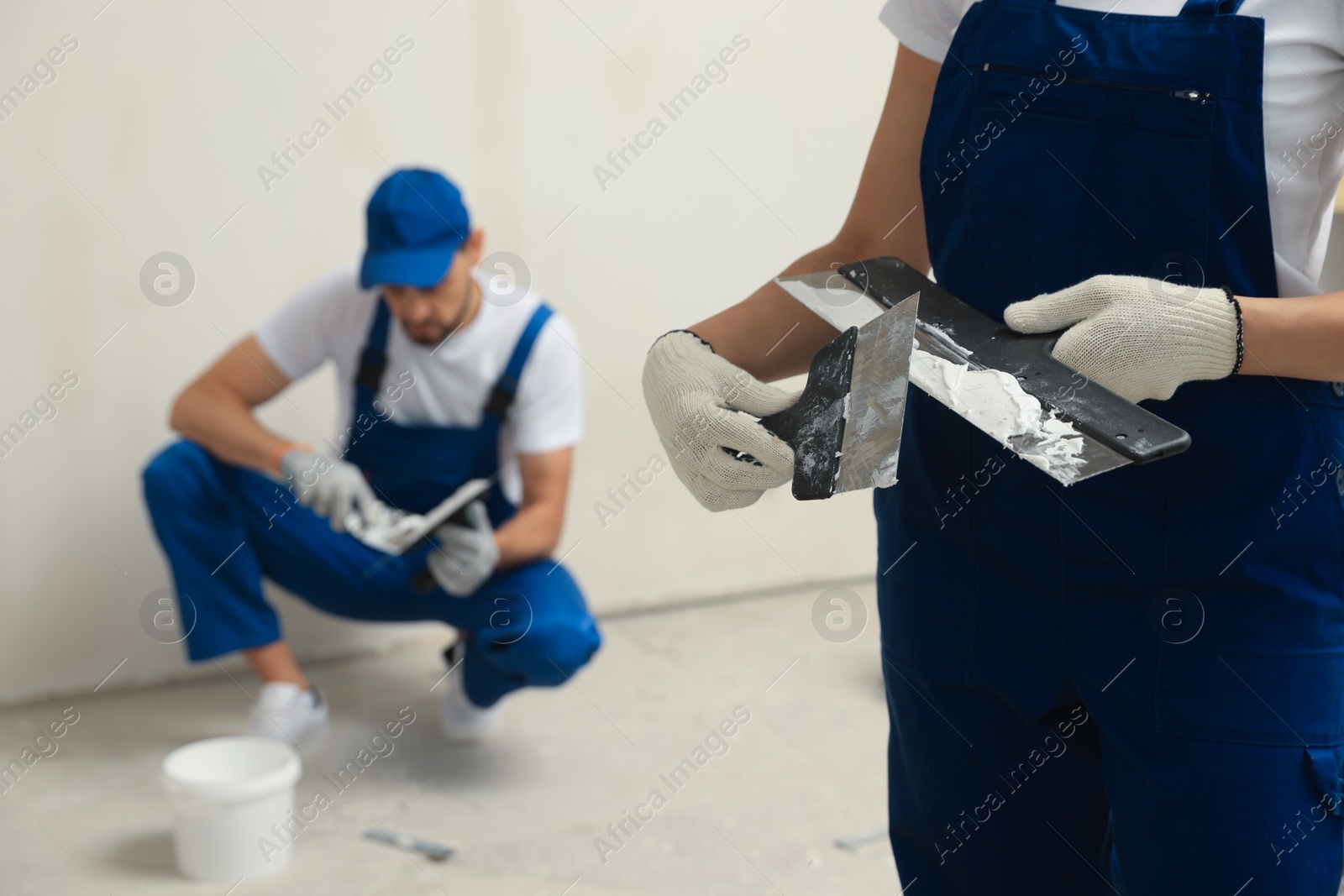 Photo of Professional workers with putty knives near wall indoors, closeup