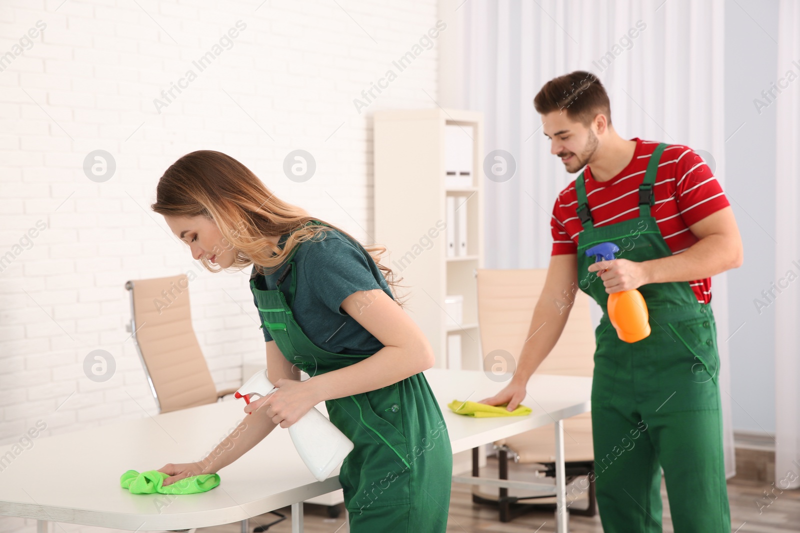 Photo of Professional janitors cleaning table in office. Hired help