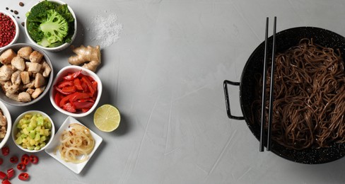 Wok with noodles, chicken and other products on light grey table, flat lay. Space for text