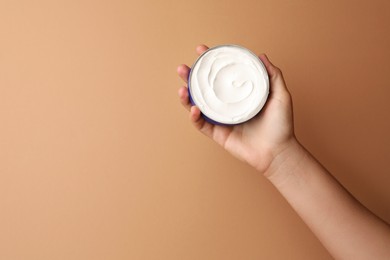 Woman holding jar of face cream on beige background, closeup. Space for text