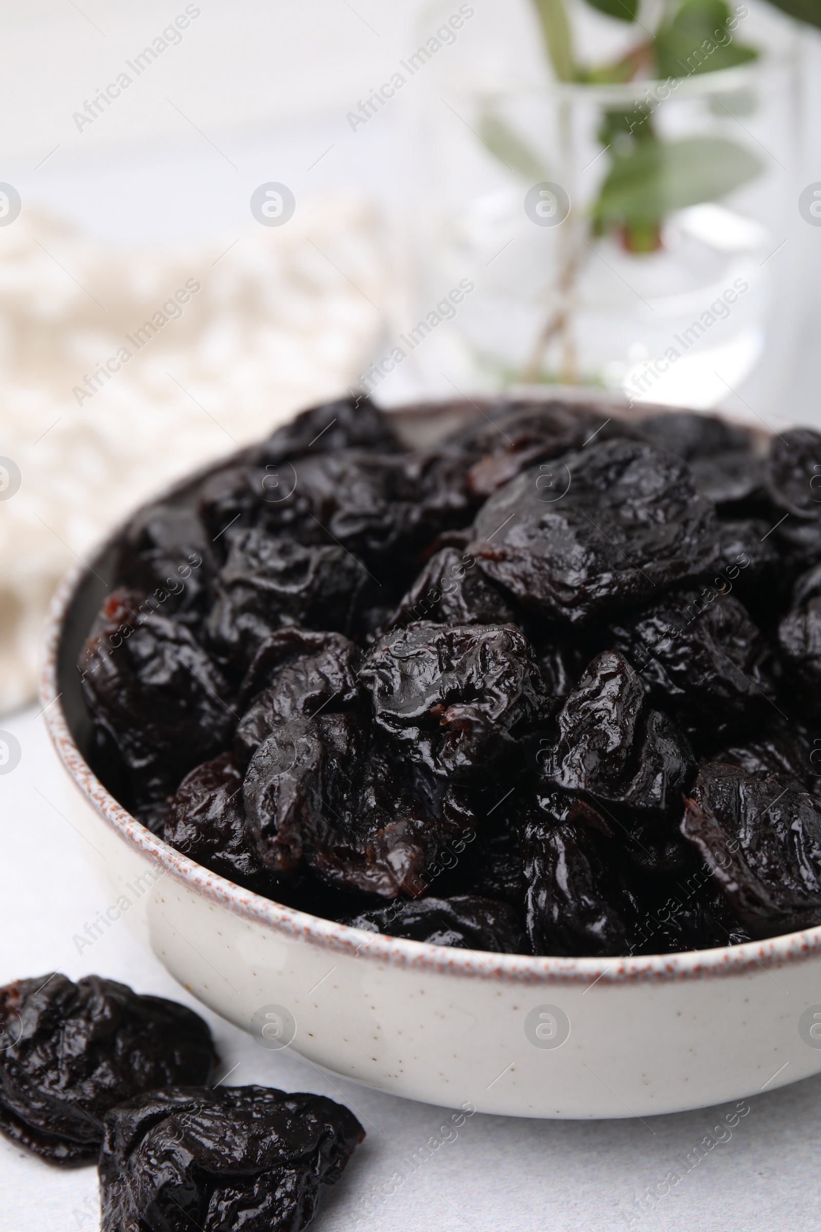 Photo of Bowl with sweet dried prunes on light table, closeup