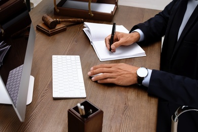 Photo of Male lawyer working with computer and notebook at table, closeup