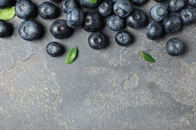 Photo of Tasty fresh blueberries and leaves on grey stone background, top view with space for text