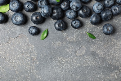 Tasty fresh blueberries and leaves on grey stone background, top view with space for text