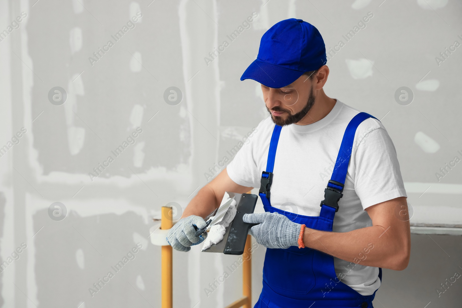 Photo of Professional worker with putty knives and plaster near wall. Space for text