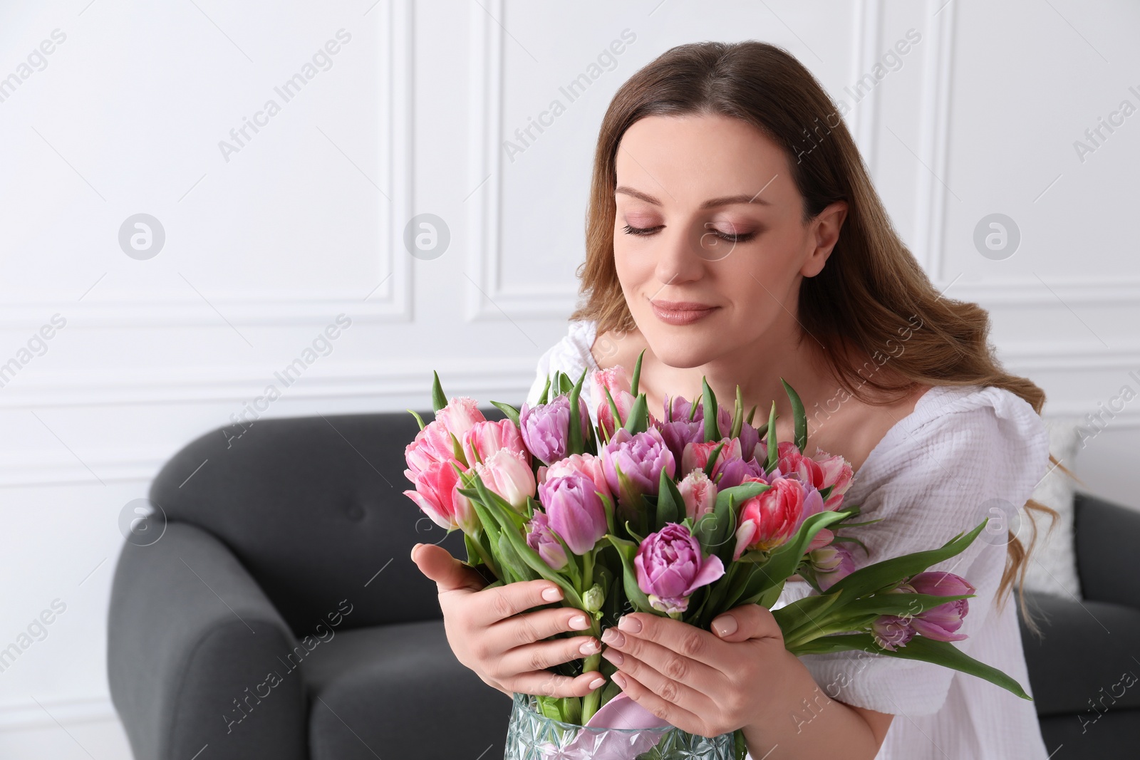 Photo of Woman smelling bouquet of beautiful tulips indoors. Space for text