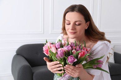 Photo of Woman smelling bouquet of beautiful tulips indoors. Space for text
