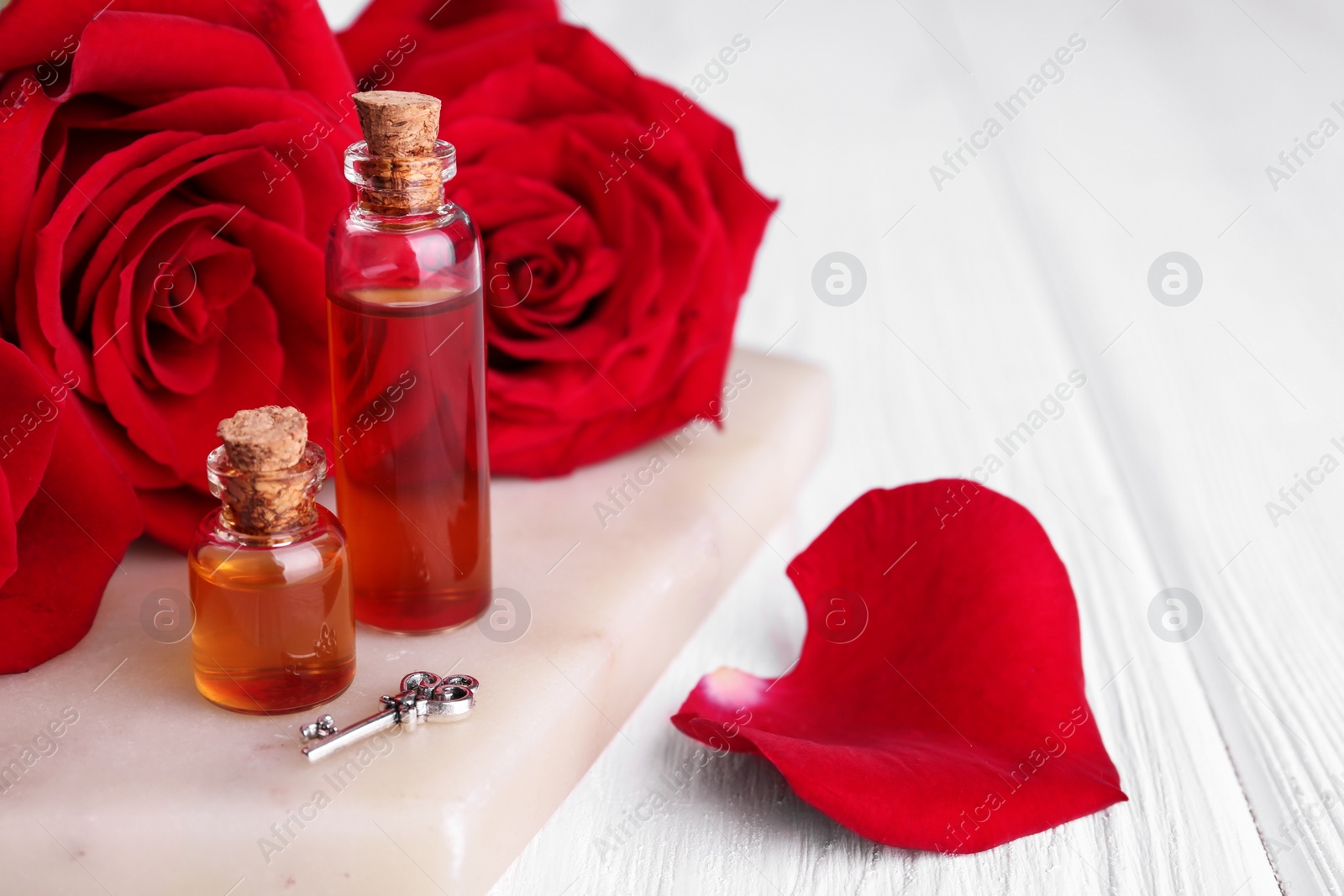 Photo of Bottles of love potion, red rose flowers and small key on white wooden table, closeup. Space for text