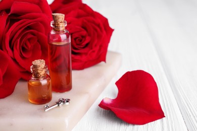 Bottles of love potion, red rose flowers and small key on white wooden table, closeup. Space for text