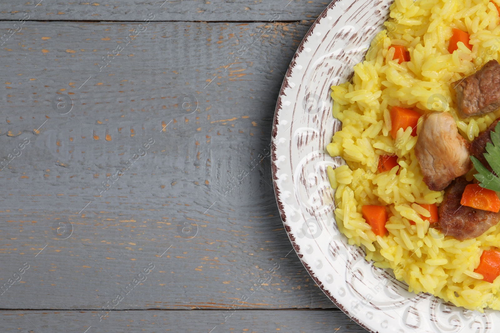 Photo of Delicious pilaf with meat on grey wooden table, top view. Space for text