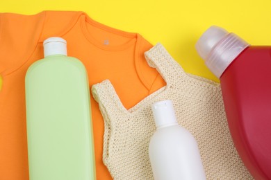 Photo of Bottles of laundry detergents and baby clothes on yellow background, flat lay