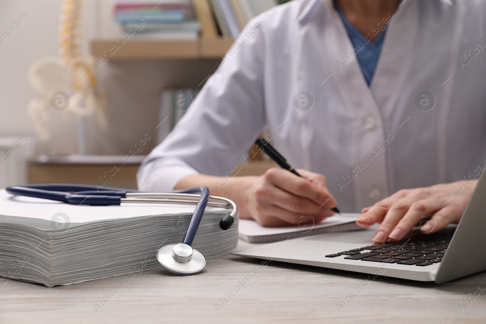 Photo of Doctor making notes from laptop at table indoors, closeup. Medical education