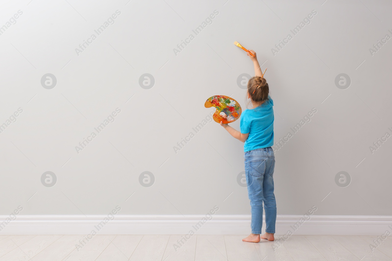 Photo of Little girl painting on light grey wall indoors, back view. Space for text