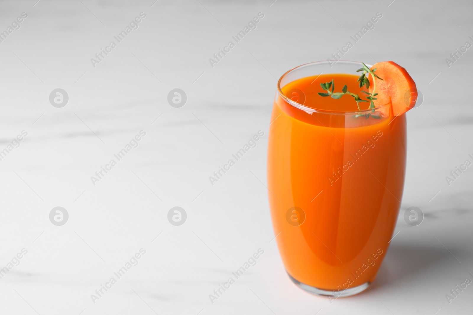 Photo of Glass with healthy carrot juice on white marble table. Space for text