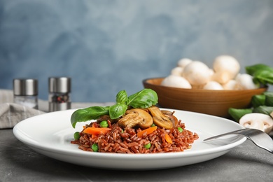 Photo of Plate of tasty brown rice with vegetables and mushrooms on grey table