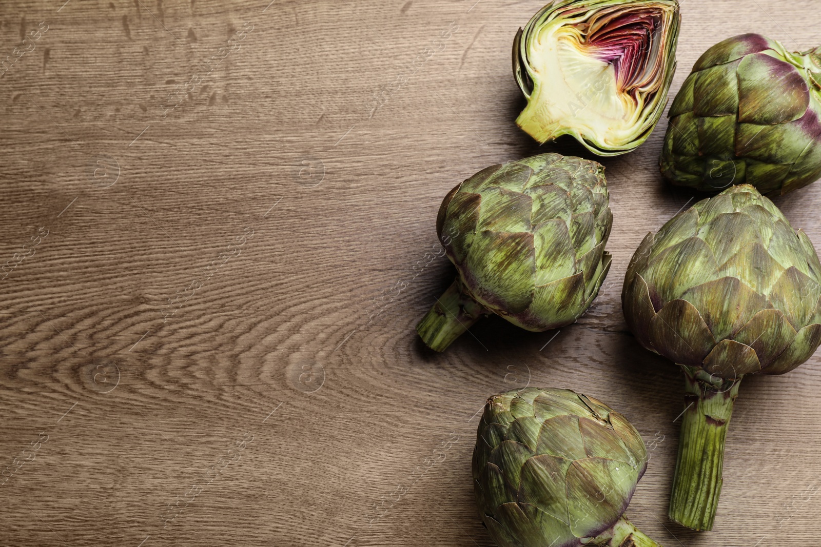 Photo of Cut and whole fresh raw artichokes on wooden table, flat lay. Space for text