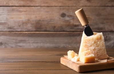 Photo of Delicious parmesan cheese with knife on wooden table. Space for text