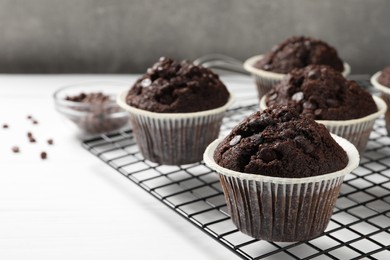 Tasty chocolate muffins and cooling rack on white table, closeup