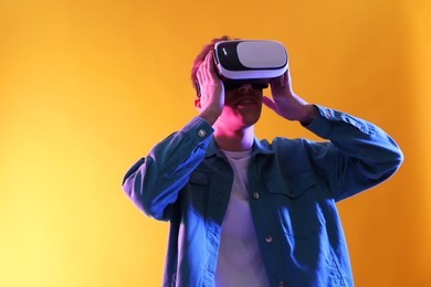 Young man with virtual reality headset on yellow background. Space for text