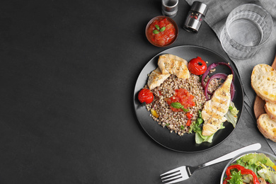 Photo of Tasty buckwheat porridge with meat and vegetables on black table, flat lay. Space for text