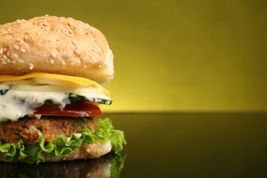 Photo of Delicious vegetarian burger on mirror surface against olive background, closeup. Space for text