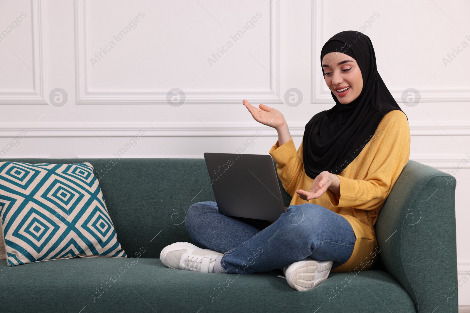 Photo of Muslim woman in hijab using video chat on laptop indoors. Space for text