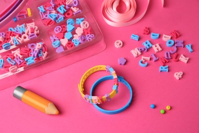 Photo of Handmade jewelry kit for kids. Colorful beads, ribbon and bracelets on bright pink background, above view