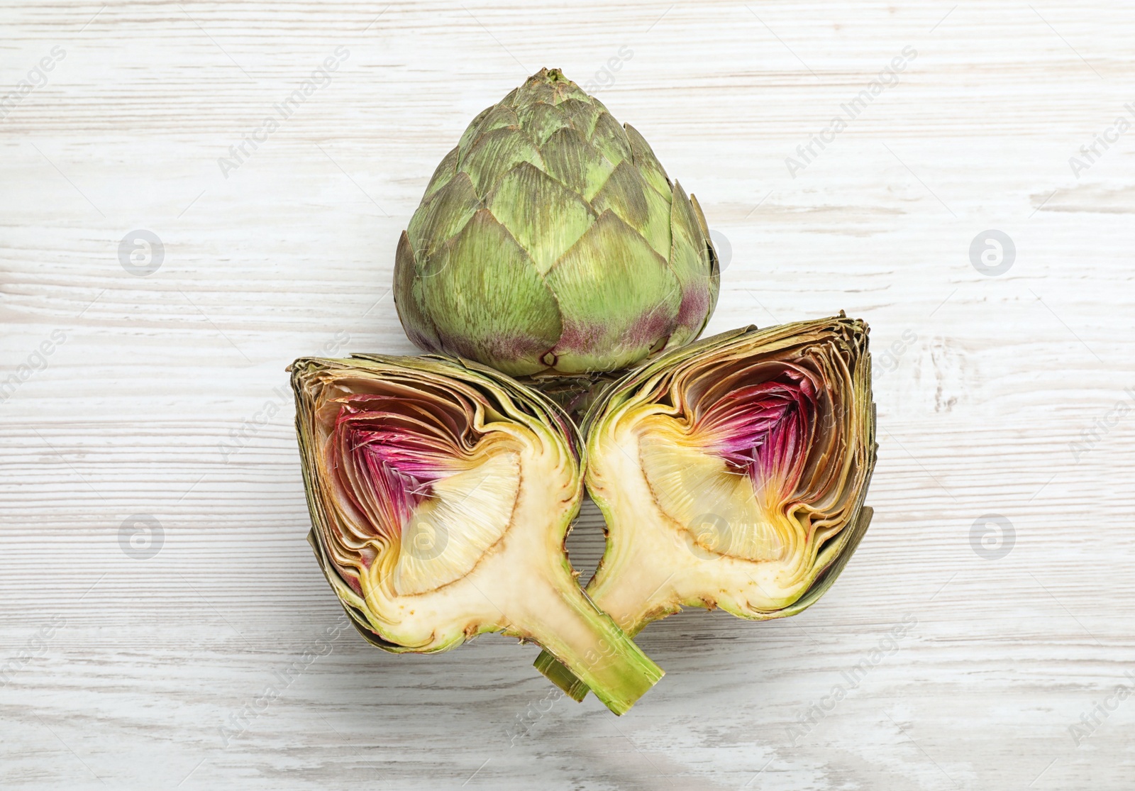 Photo of Cut and whole fresh raw artichokes on white wooden table, flat lay