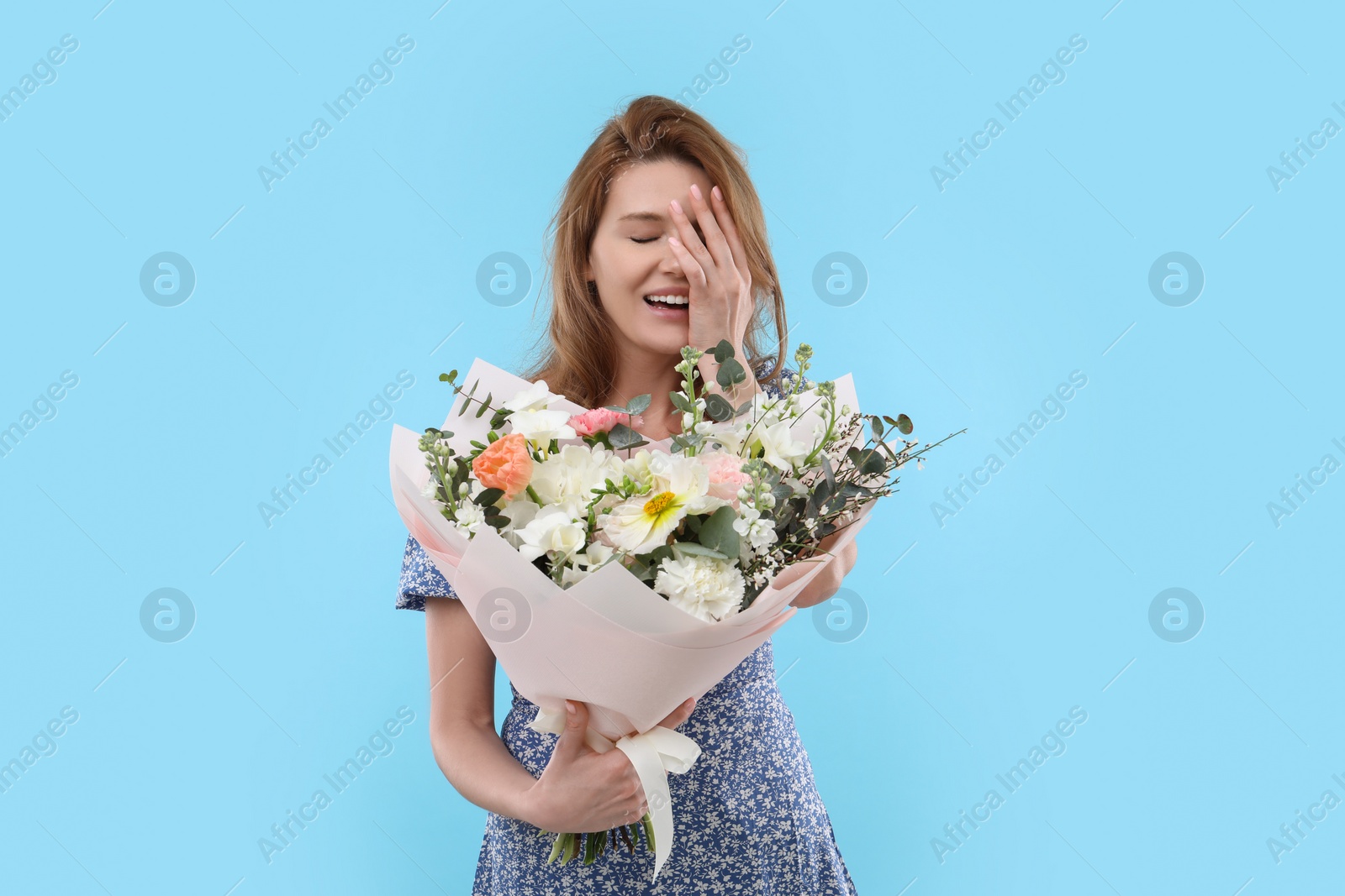 Photo of Happy woman with bouquet of beautiful flowers on light blue background