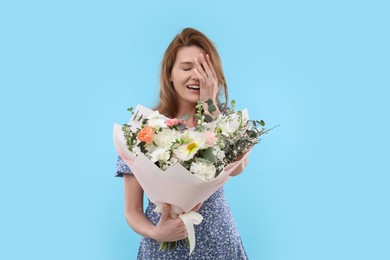 Photo of Happy woman with bouquet of beautiful flowers on light blue background