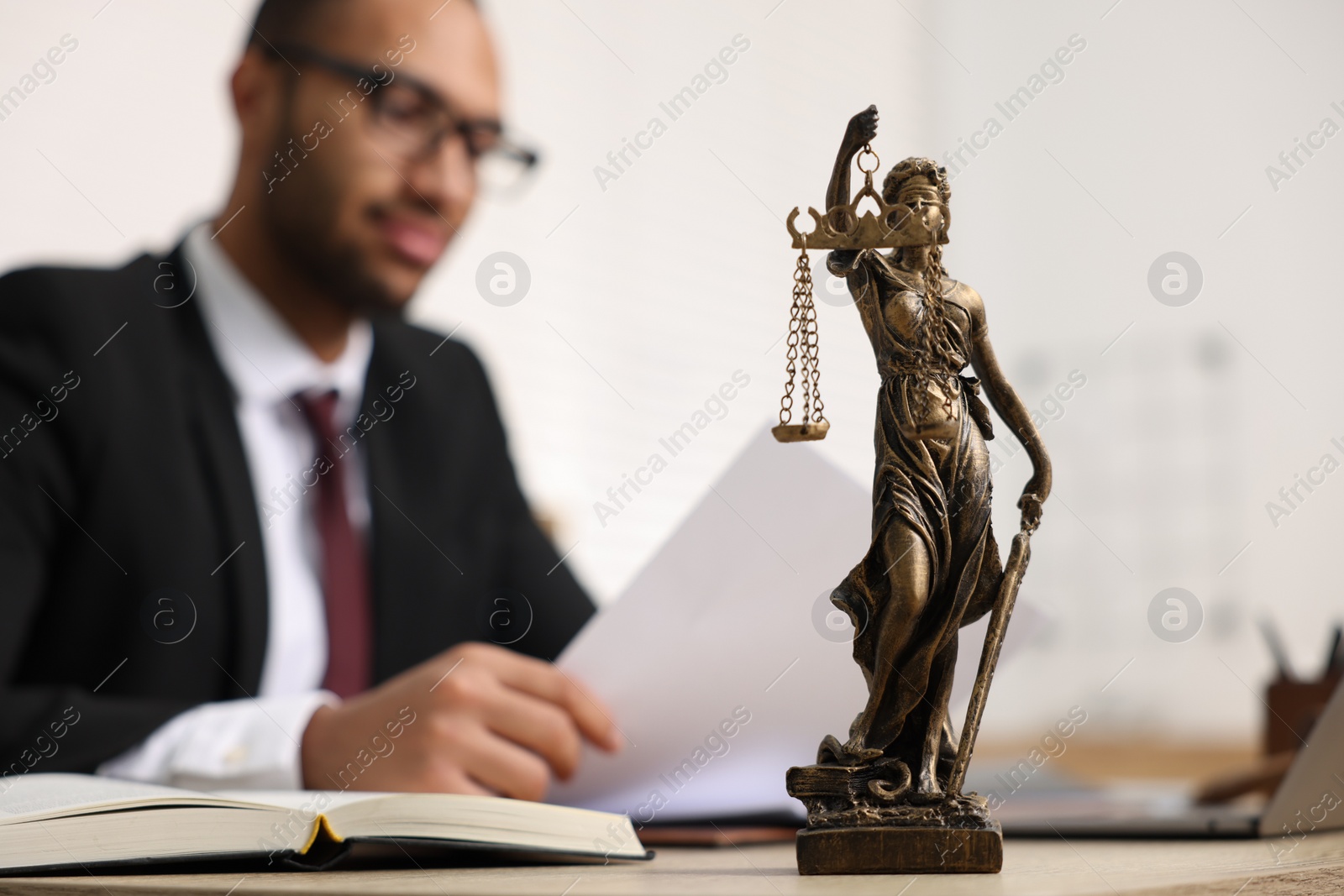 Photo of Lawyer working with document at table in office, focus on statue of Lady Justice