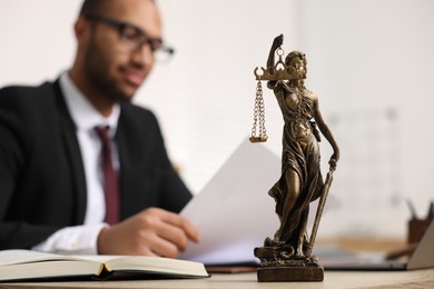 Photo of Lawyer working with document at table in office, focus on statue of Lady Justice