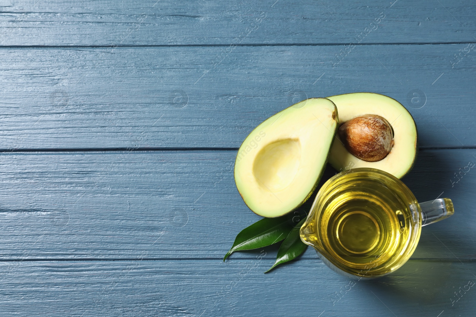 Photo of Gravy boat with oil and ripe fresh avocado on wooden table, top view