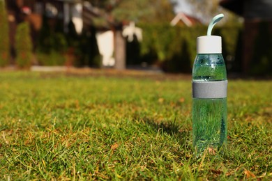 Photo of Glass bottle of fresh water on green grass outdoors. Space for text