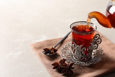 Photo of Pouring traditional Turkish tea from pot into glass on table. Space for text