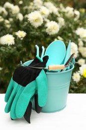 Gardening gloves and bucket with different tools on white wooden table outdoors