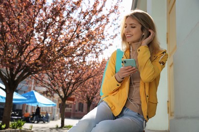 Young woman listening to audiobook on city street. Space for text